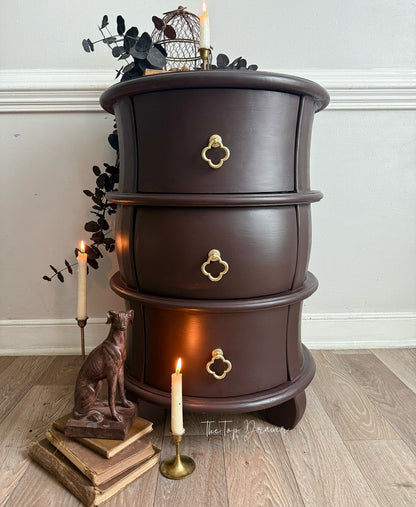 Wooden side table with three drawers, candles, and decorative items on a wooden floor.