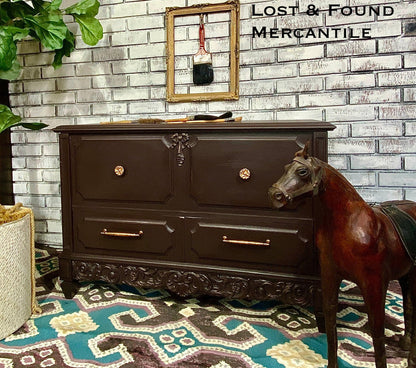 Dark wooden dresser with gold handles against a brick wall, with a horse model in front.