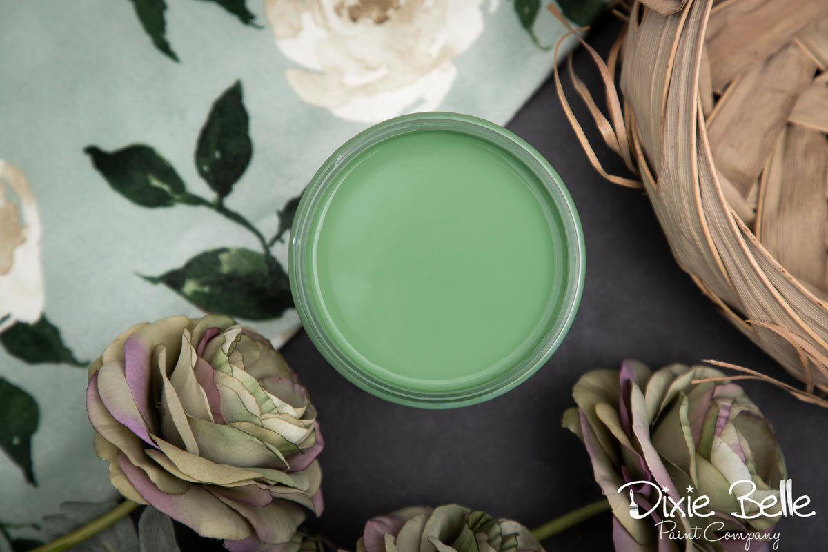 Green paint can on a dark surface with flowers and a woven basket in the background