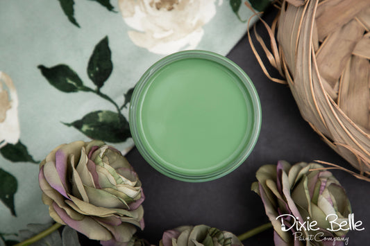 Green paint can on a dark surface with flowers and a woven basket in the background