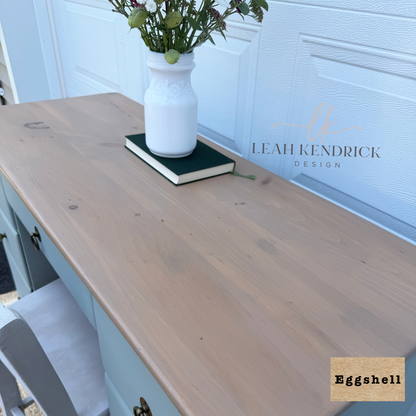 A light natural wood vanity top or desk surface shown in a real interior setting, with a white vase and book on top. The scene includes a white paneled door in the background and a visible Leah Kendrick Design watermark; a small label in the corner reads Eggshell.