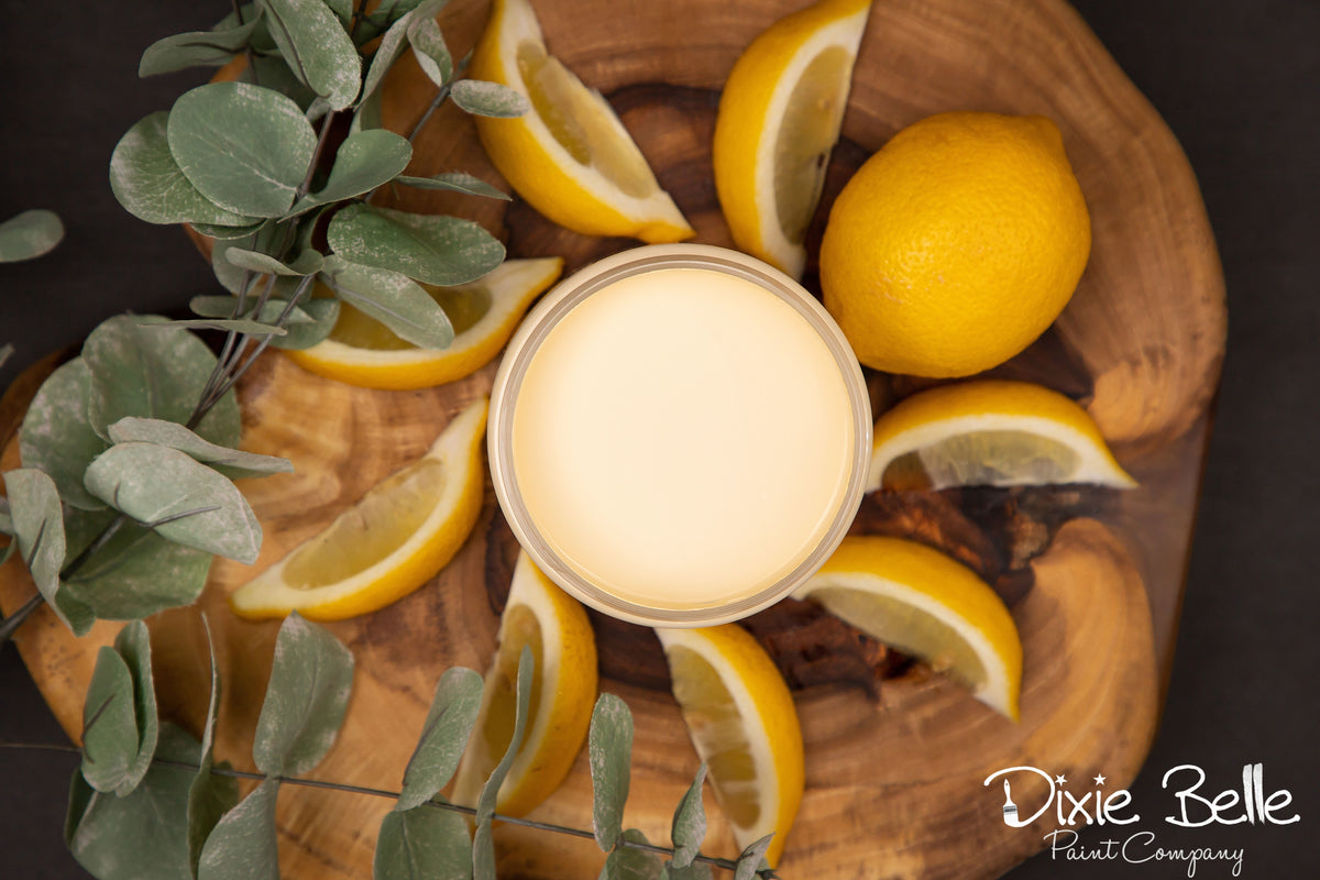 Wooden bowl with sliced lemons and a jar of Dixie Belle Paint color Lemonade on a dark background, featuring the Dixie Belle Paint Company logo.