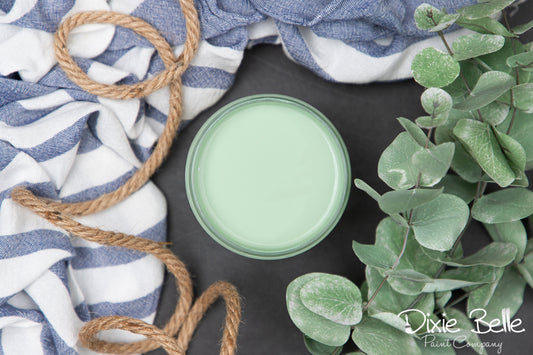 Dixie Belle Paint color Mint Julep on a dark surface with a striped cloth, twine, and green leaves in the background.
