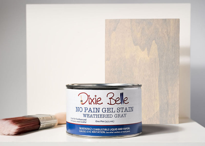 Dixie Belle No Pain Gel Stain can with a brush and stained wood panel on a gray background