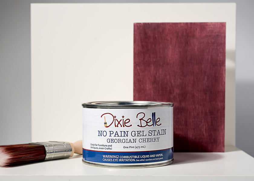 Dixie Belle No Pain Gel Stain can with brush and stained wood panel on a white background