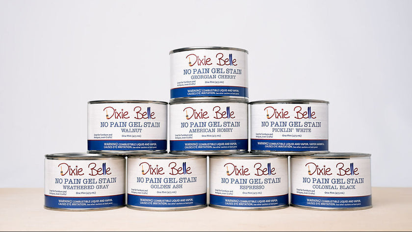 Eight Dixie Belle No Pain Gel Stain cans arranged in a pyramid stack on a light beige surface against a white background.
