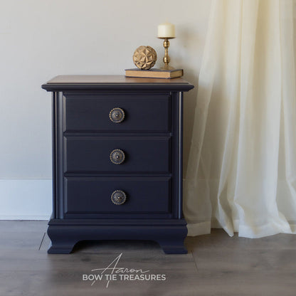 black nightstand with three drawers and decorative items on a neutral background