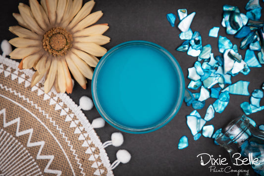 Dixie Belle Paint color Peacock with a flower and decorative elements on a dark surface, featuring the Dixie Belle Paint Company branding.