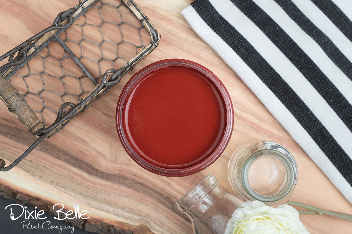 Red paint sample on a wooden surface with a black and white striped towel and a bottle of water.