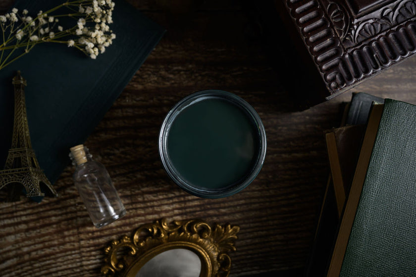 Dark green paint can on a textured surface with decorative items like a miniature Eiffel Tower and mirror.