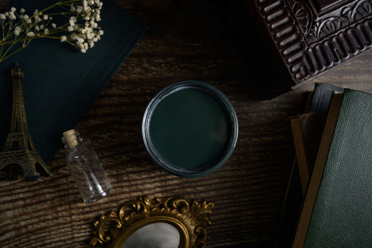 Dark green paint can on a textured surface with decorative items like a miniature Eiffel Tower and mirror.