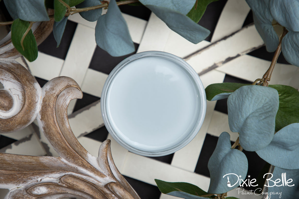 Jar of light blue paint with decorative elements and green leaves on a checkered surface