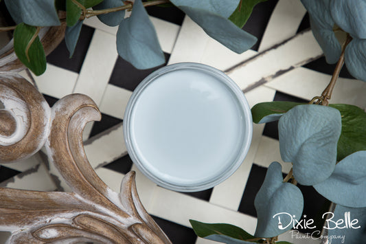 Jar of light blue paint with decorative elements and green leaves on a checkered surface