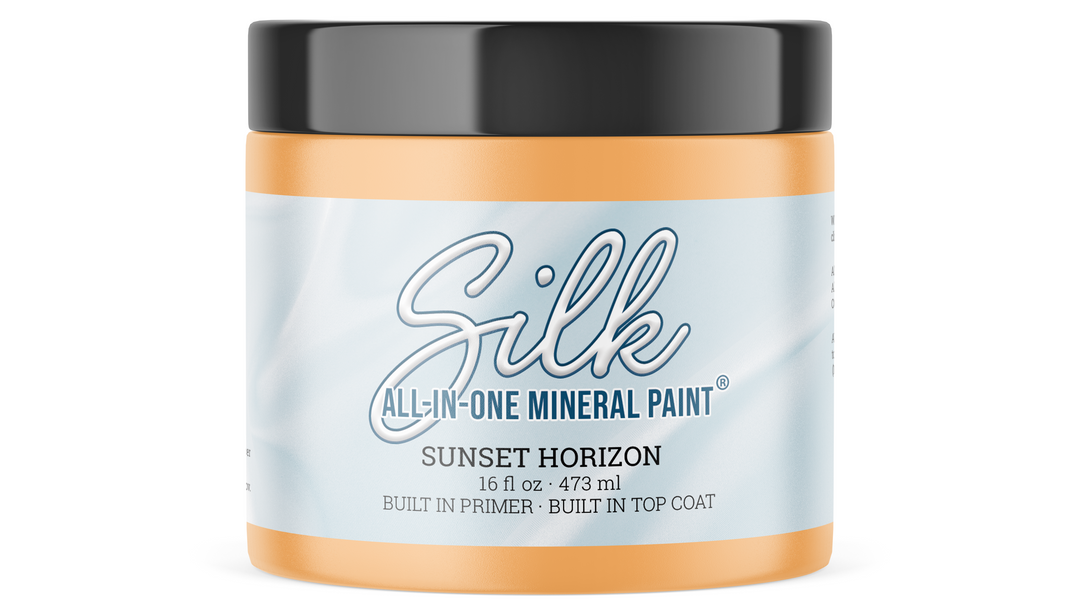 A jar of Silk All-In-One Mineral Paint in the shade Sunset Horizon, featuring a light blue and white label with a black lid and orange-brown paint visible at the top and bottom.