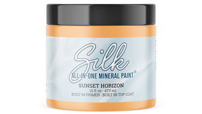 A jar of Silk All-In-One Mineral Paint in the shade Sunset Horizon, featuring a light blue and white label with a black lid and orange-brown paint visible at the top and bottom.