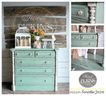Teal dresser with decorative items against a wooden wall with 'Sweet Pickins' sign.