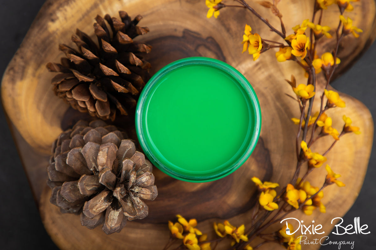 Green paint sample on a wooden surface with pine cones and yellow flowers