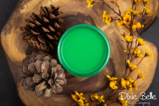 Green paint sample on a wooden surface with pine cones and yellow flowers