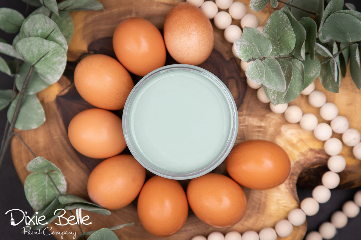 Dixie Belle paint Vintage Duck Egg can surrounded by brown eggs on a wooden surface with decorative elements.