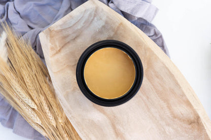 Terra Clay Paint Wheat in a black container on a wooden board with dried grasses and fabric in the background