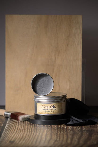 Tin of wax with a brush and black cloth on a wooden surface