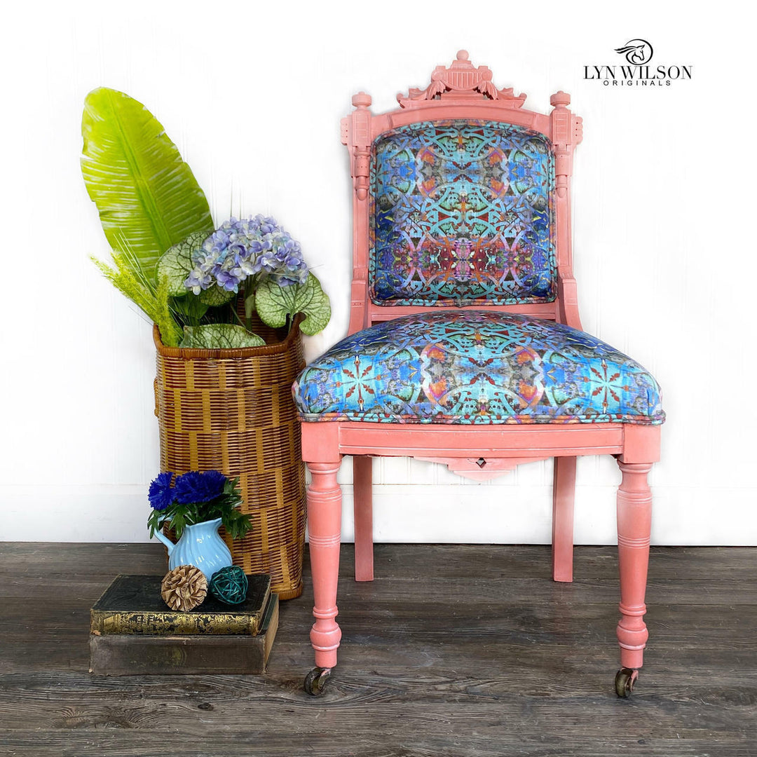 Pink chair with floral pattern next to a woven basket with plants on a wooden floor.