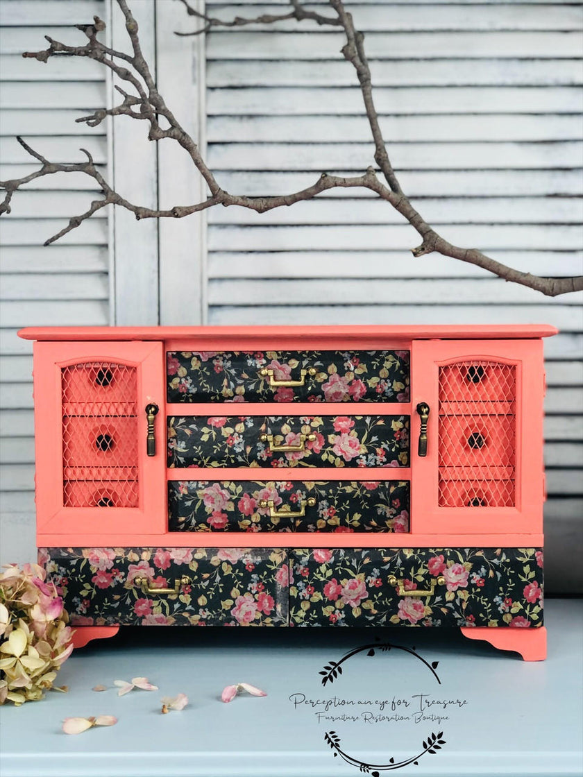 Coral and floral-patterned dresser against a gray wall with branches.