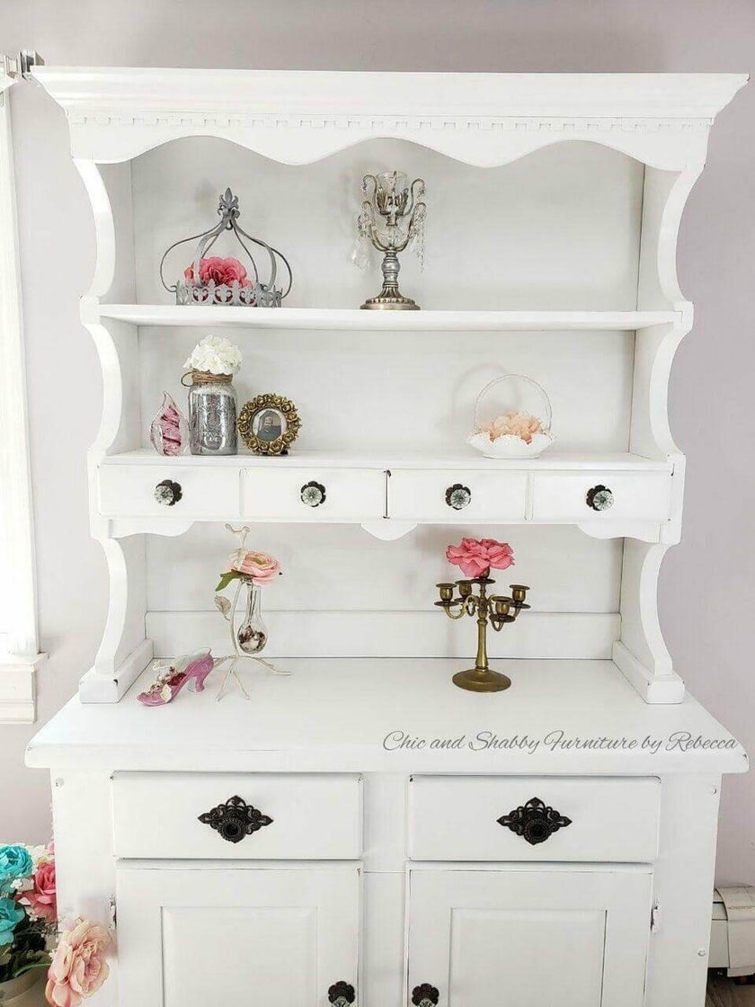 A white shabby-chic style wooden hutch cabinet with decorative shelves and drawers, styled with pink roses and silver candle holders, with a watermark 'Chic and Shabby Furnitures by Rebecca' on the front.
