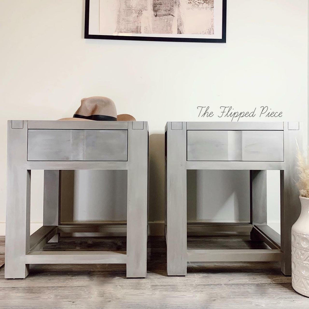 Two wooden nightstands with a hat on one of them, against a neutral wall.