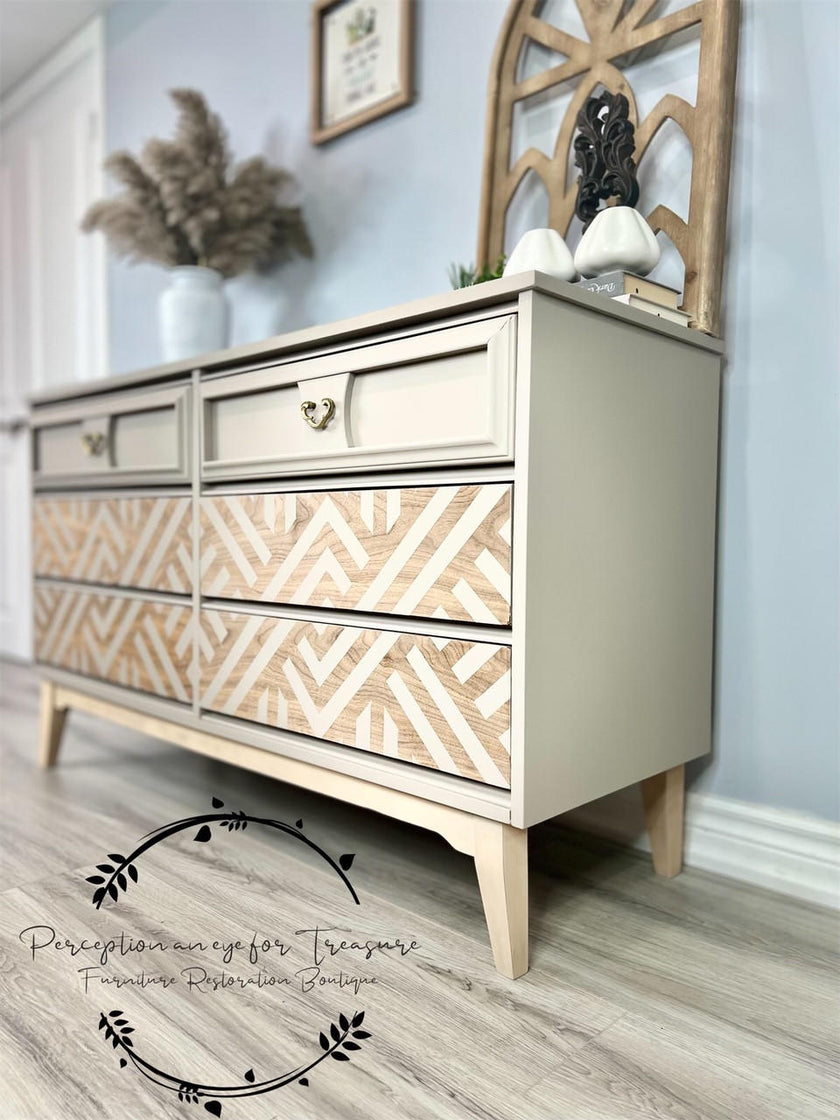 A mid-century modern dresser with a beige painted frame and natural wood drawer fronts featuring a geometric chevron pattern, styled in a home interior setting.