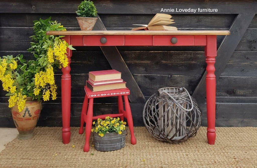 Red wooden table with yellow flowers, a stool, and decorative items against a wooden wall.