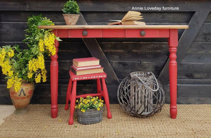 Red wooden table with yellow flowers, a stool, and decorative items against a wooden wall.