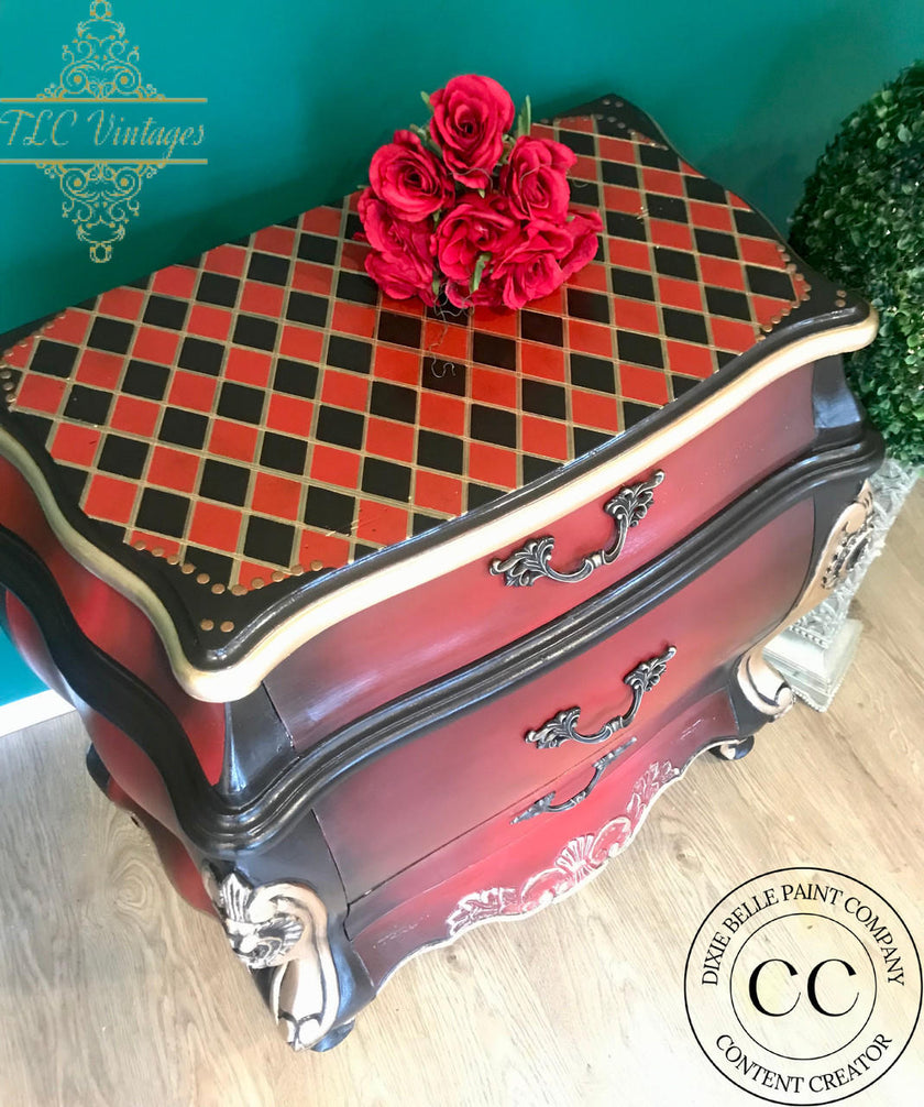 A vintage-style wooden chest of drawers with a red and black checkered top, decorated with red roses, set against a teal wall and light wood floor. Watermarks for TLC Vintage and Indirelle Paint Company are visible.
