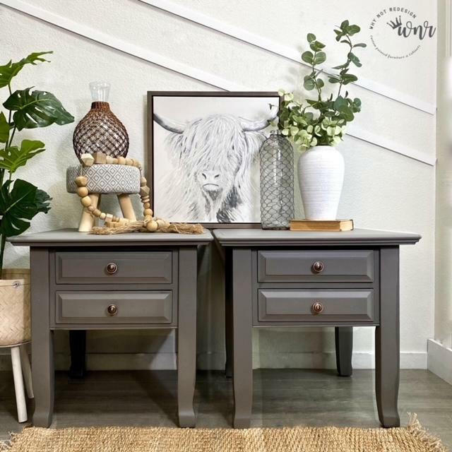 Two matching gray painted wooden nightstands with two drawers and round metal knobs, styled in a home interior setting with plants, a picture frame, and decorative vases.