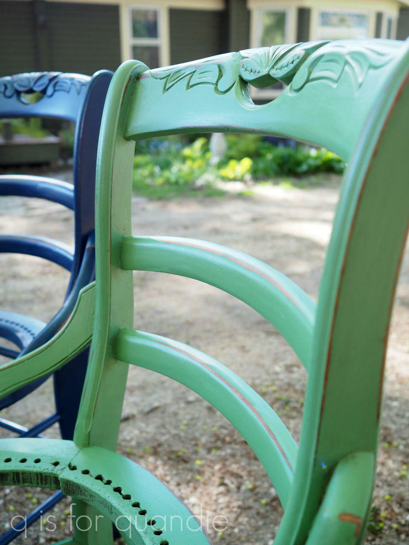 Close-up of a green wooden chair with decorative backrest in an outdoor setting.