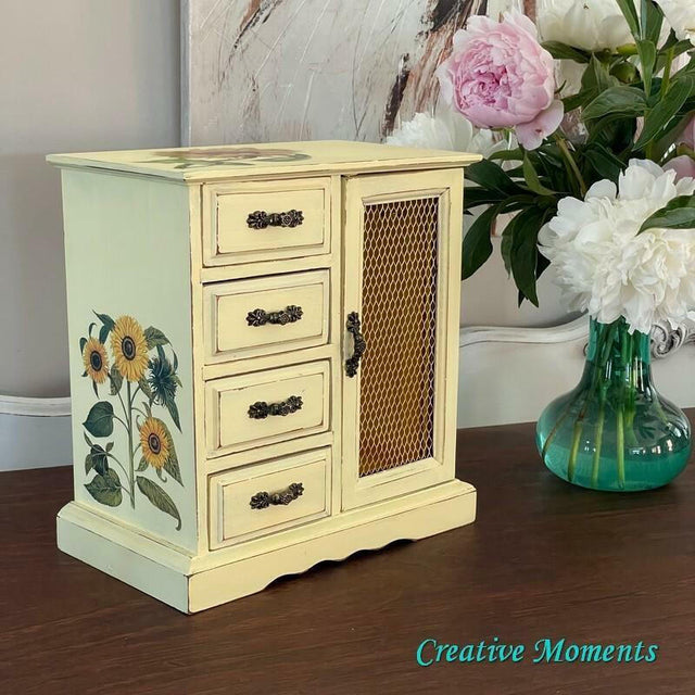 Small wooden cabinet with floral design on a table next to a vase of flowers.