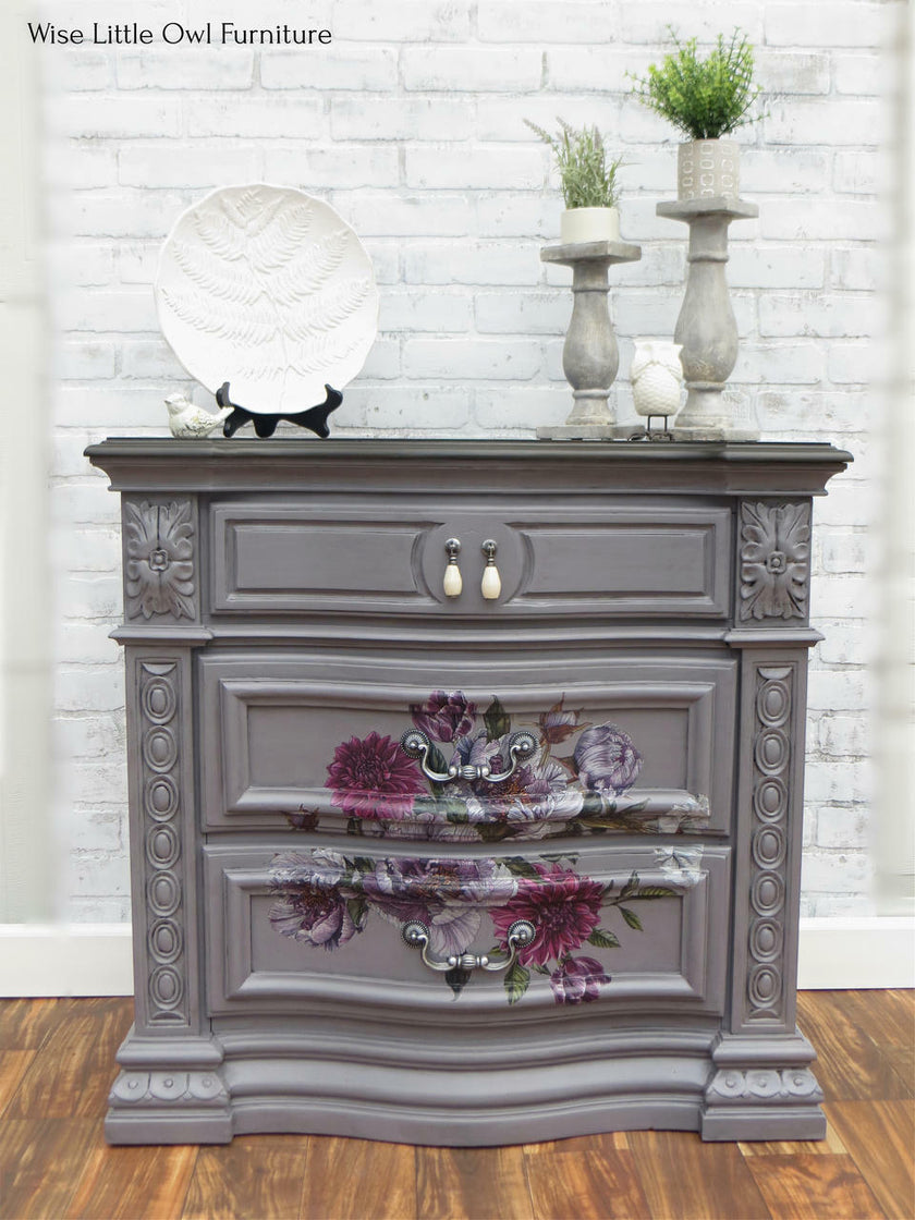 Decorative gray dresser with floral design against a white brick wall.