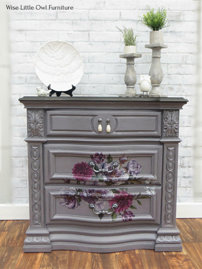Decorative gray dresser with floral design against a white brick wall.