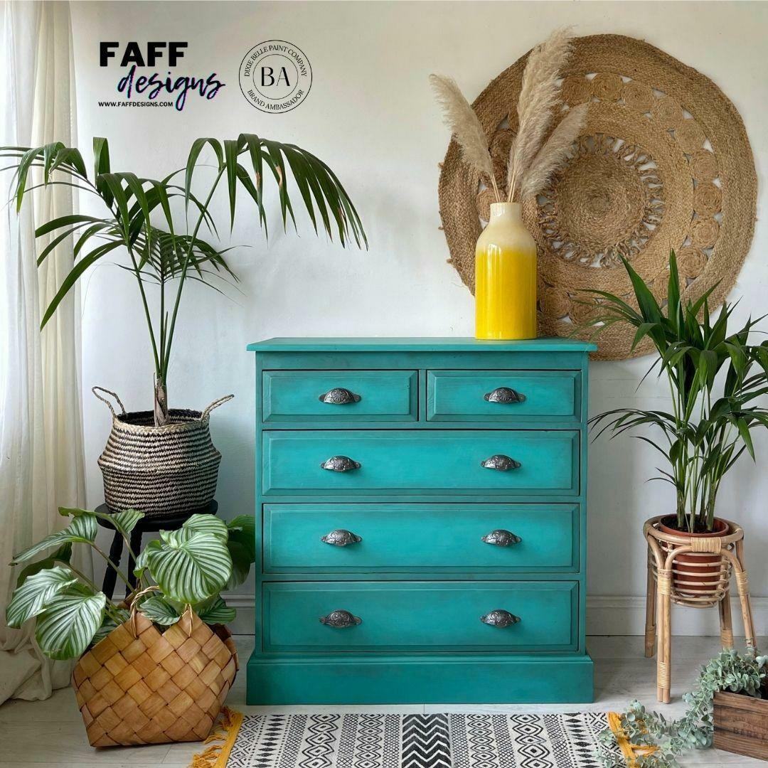 Turquoise dresser with decorative items in a room with plants and a rug.