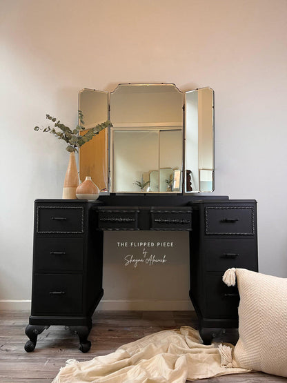 Black vanity with a large mirror and decorative items on a wooden floor.