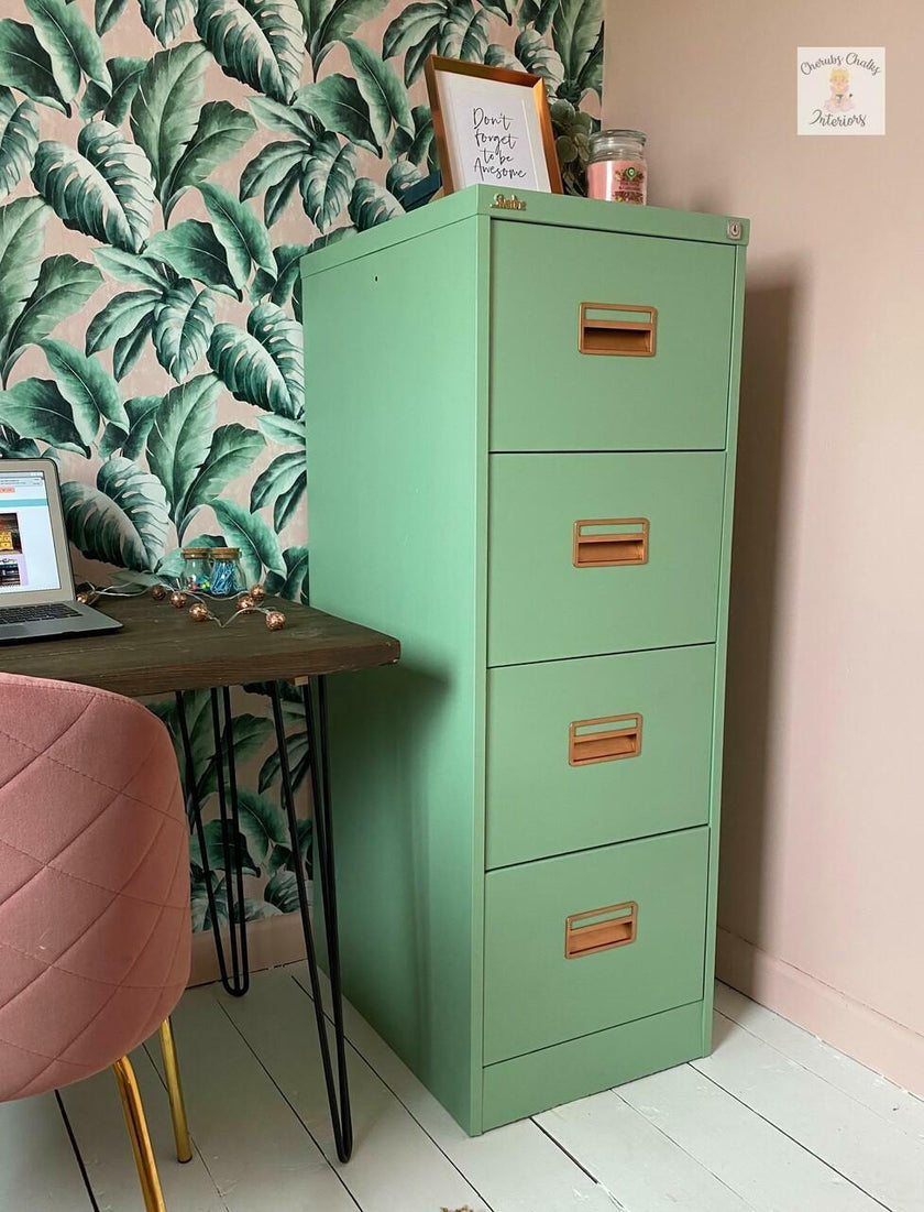 Green metal filing cabinet next to a pink chair and desk with leaf-patterned wallpaper.