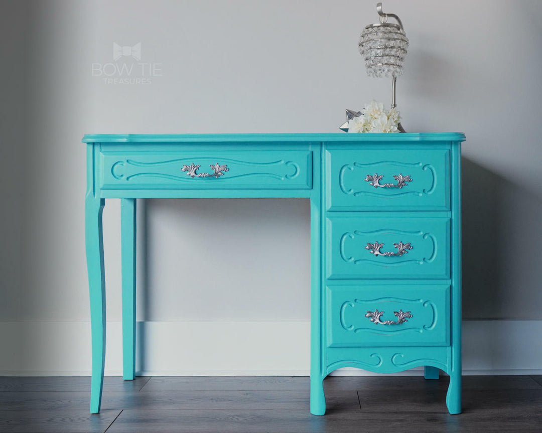 Turquoise desk with decorative handles against a gray wall