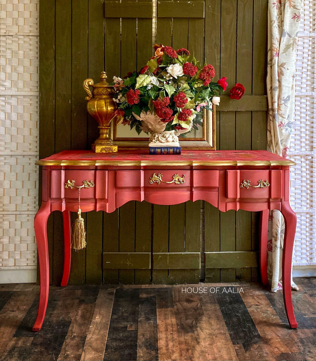 Red and gold console table with decorative items against a wooden wall.