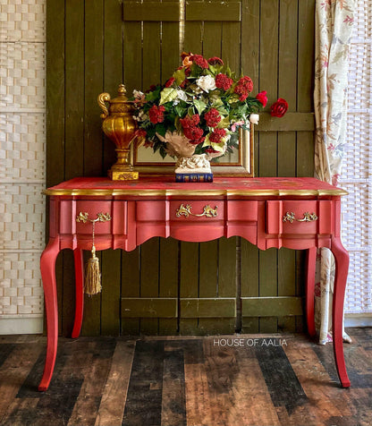 Red and gold console table with decorative items against a wooden wall.