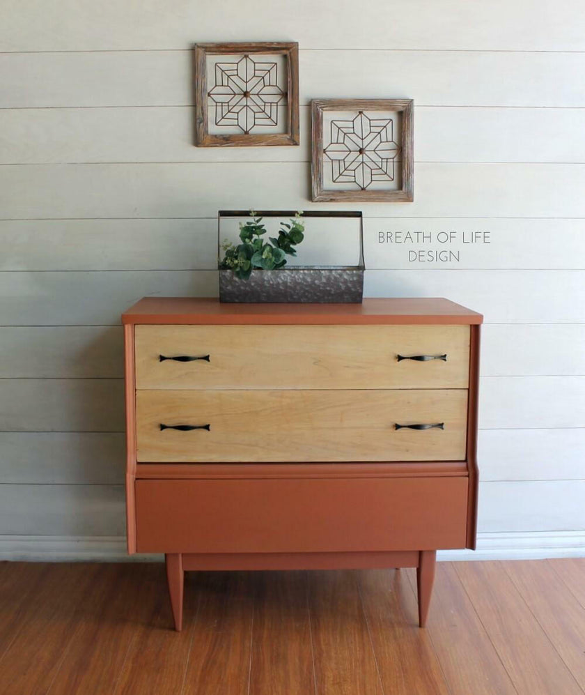 Wooden dresser with decorative items on a wooden floor and white wall.