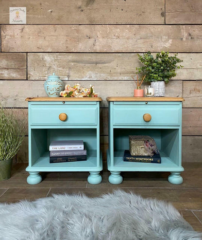 A pair of turquoise painted nightstands with light wood tops and round wooden knobs, styled with books, a ceramic jar, and a small plant against a rustic wood plank wall.