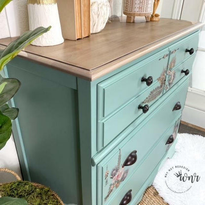Teal dresser with floral decal and wooden top in a room setting.