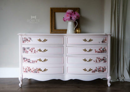 White dresser with floral decors on drawers against a neutral wall.