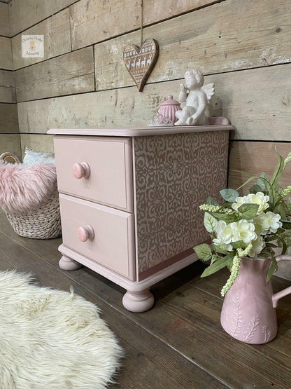 Pink patterned nightstand with decorative items against a wooden wall.