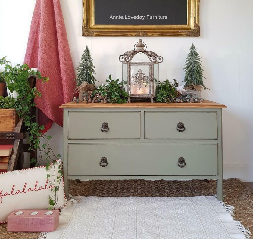 Green dresser with decorative items in a room with a red curtain and framed picture.